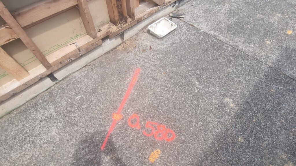 Orange spray paint marking on concrete floor for plumbing installation.